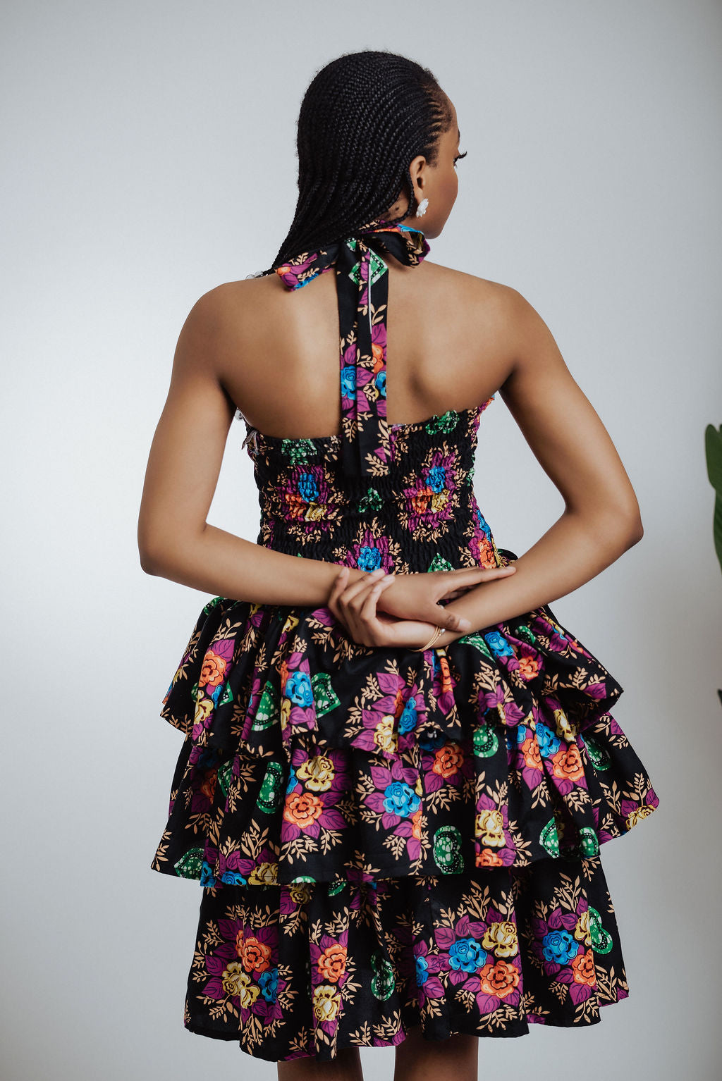 Woman wearing a black floral dress with colorful flowers on a plain background back view