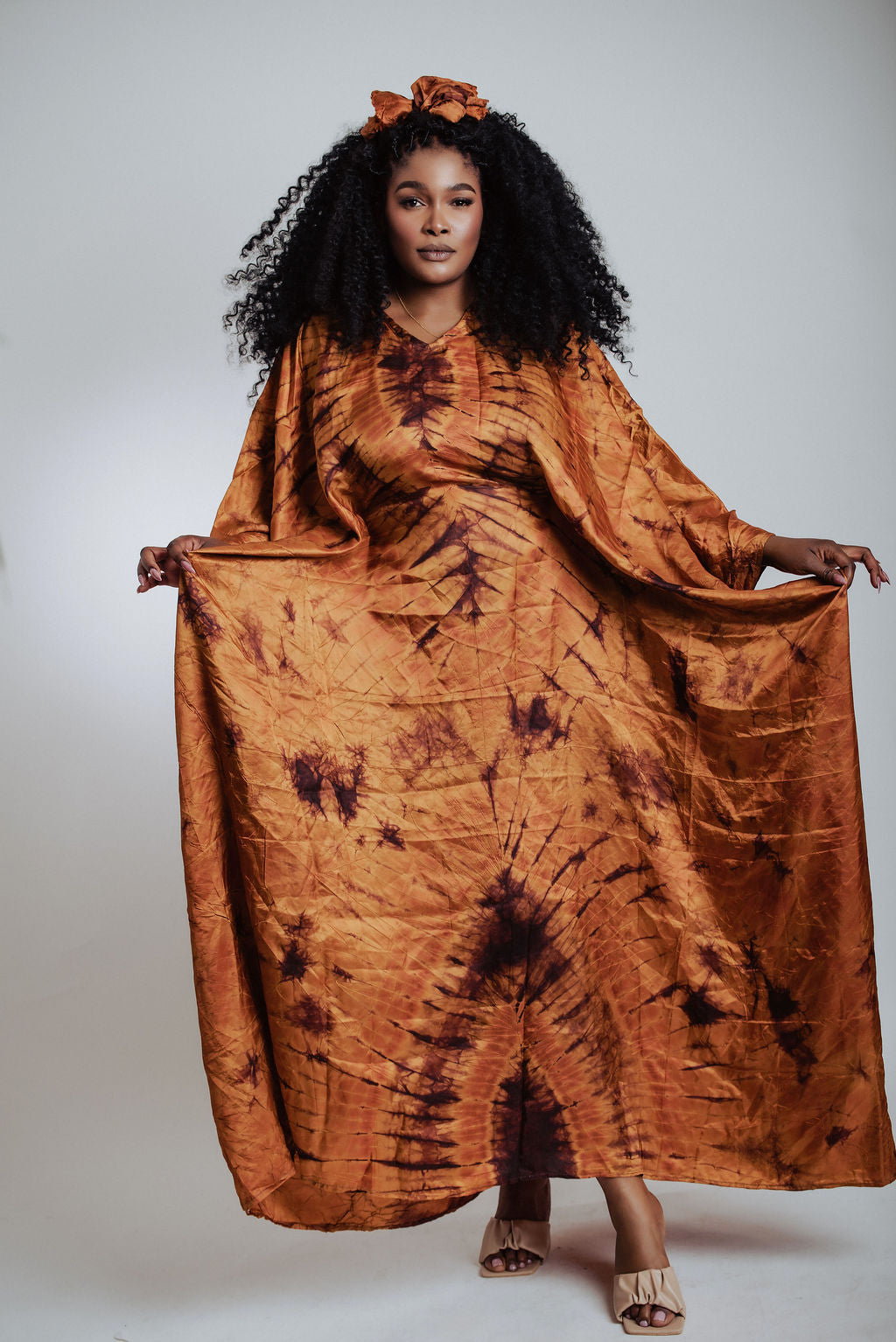 Woman wearing a long, silk tie-dye brown dress against a plain background