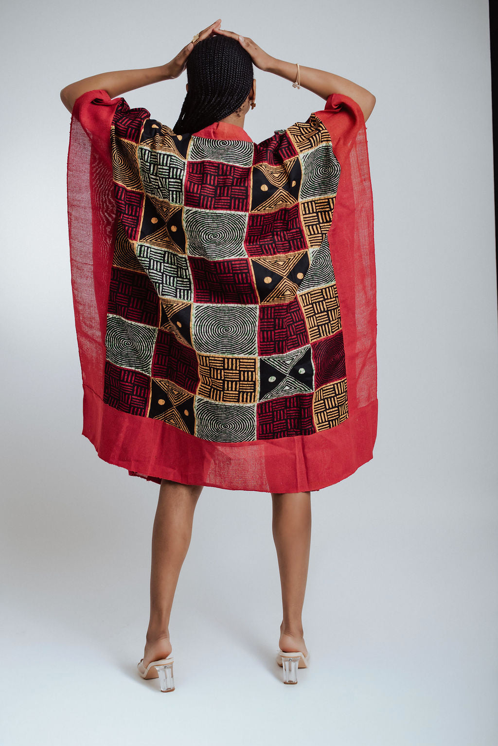 Woman wearing a red dress with yellow, white and black patterns on a white background - back view