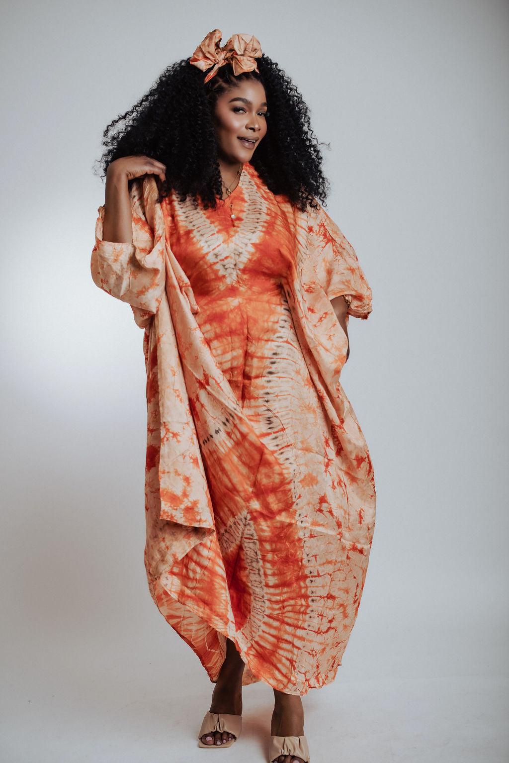 Woman wearing an orange tie-dye dress with a plain background