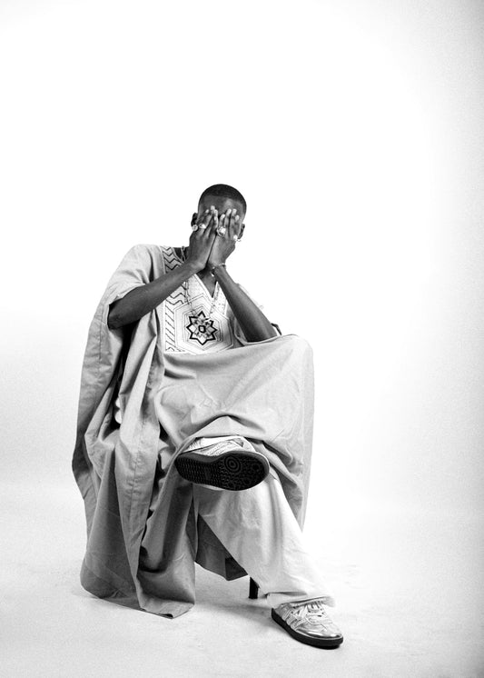 Man in traditional african attire sitting with hands covering face.