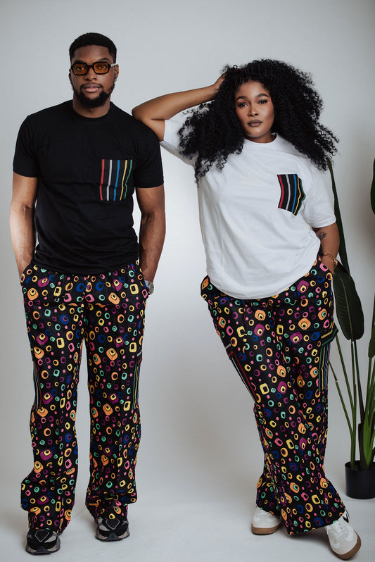 Male and female models wearing patterned African print cargo pants with black and white pocket T-shirts against a white background with a plant