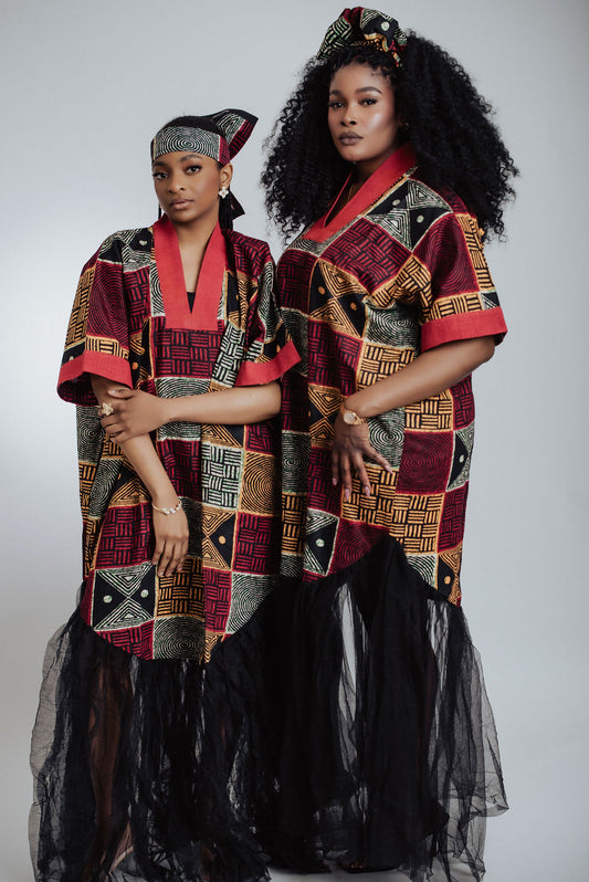 Two women wearing traditional African print dress/boubou with a geometric pattern and black tulle on a plain background