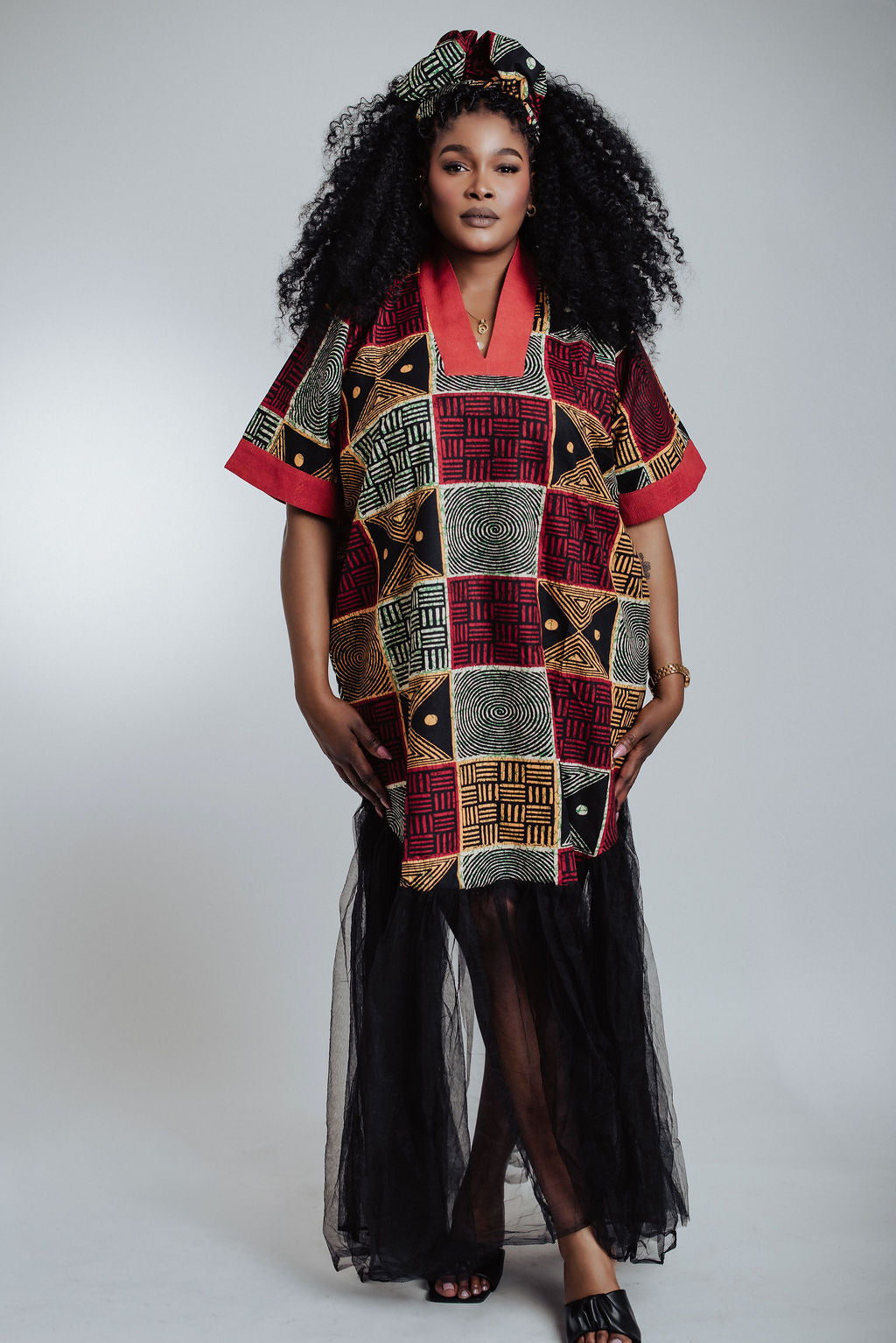 Woman wearing a geometric African print dress/boubou with black Tulle against a white background