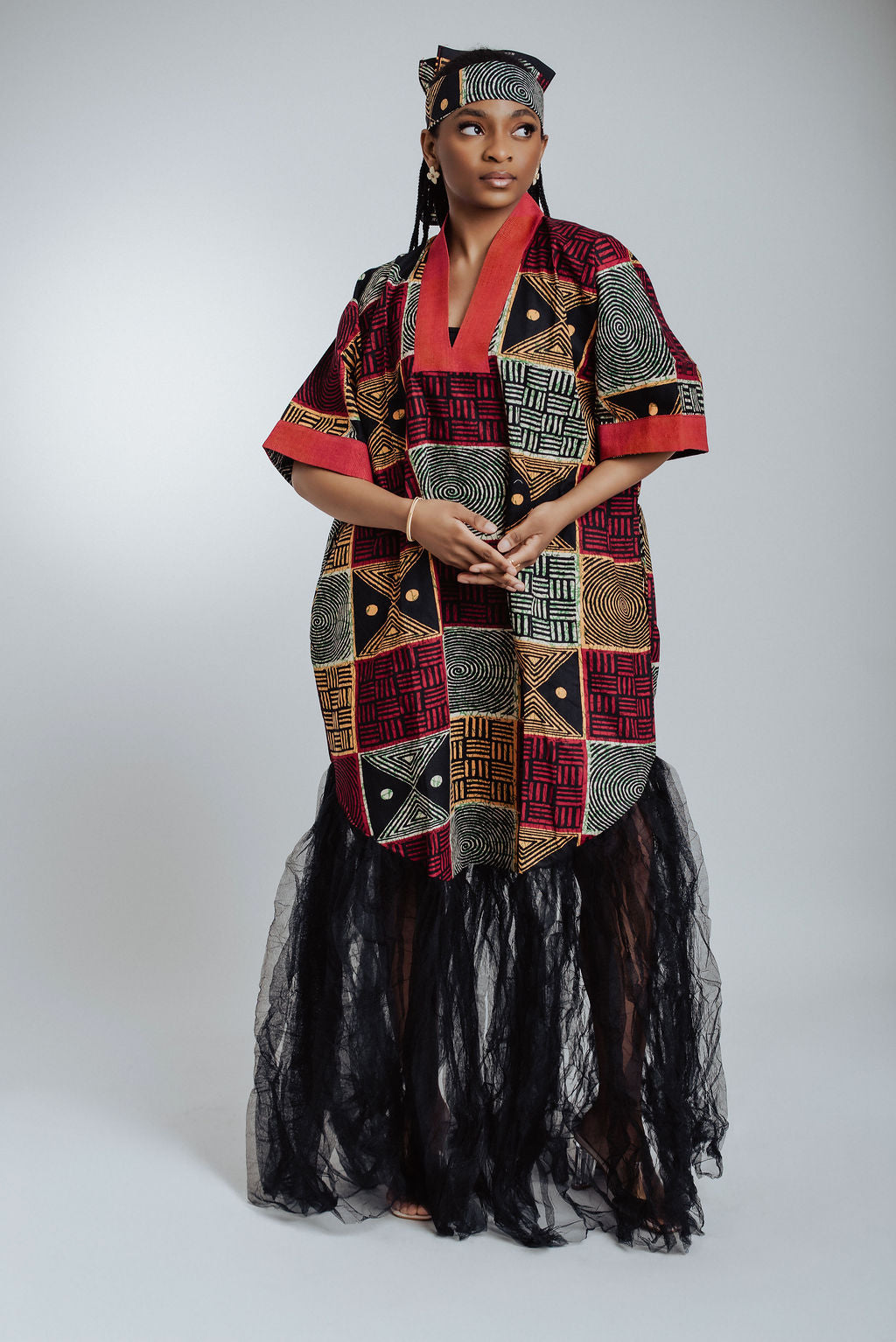 Woman wearing a geometric African print dress/boubou with black Tulle against a white background