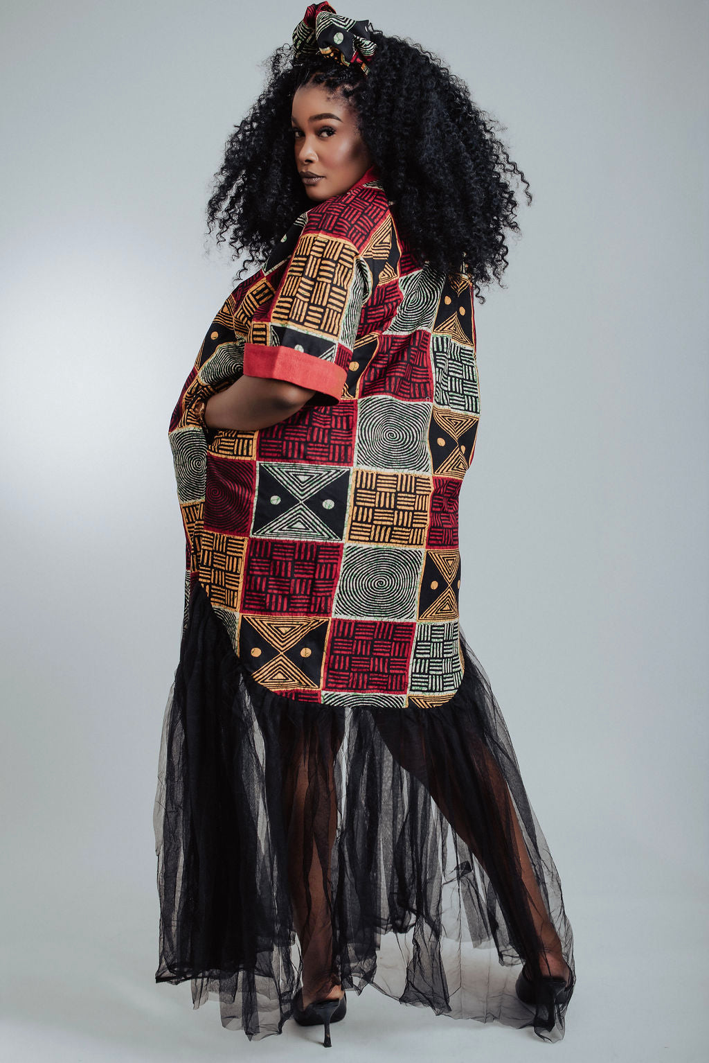 Back view of woman wearing a geometric African print dress/boubou with black Tulle against a white background