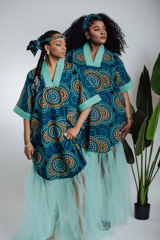 Two women wearing teal traditional African print dress/boubou with a geometric pattern and tulle on a plain background