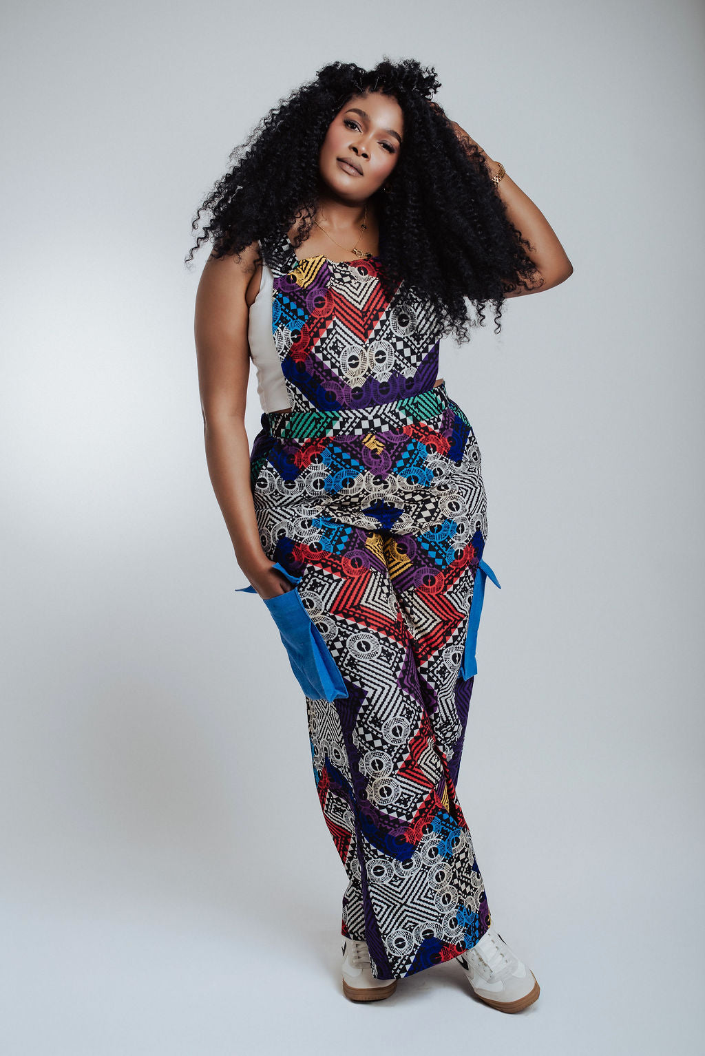 A woman wearing a handmade geometric African print jumpsuit with vibrant colors and blue side-pockets. This piece showcases traditional Ankara textiles reinvented for a modern wardrobe. The styling is versatile and bold, designed for the ZS Collective woman who values culture, comfort, and intentional craftsmanship.