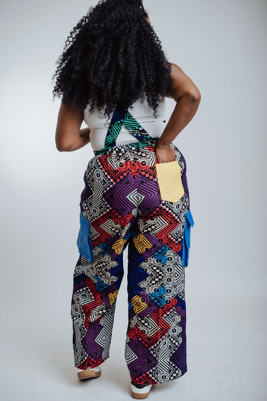 A woman wearing a handmade geometric African print jumpsuit with vibrant colors and yellow back-pocket. This piece showcases traditional Ankara textiles reinvented for a modern wardrobe. The styling is versatile and bold, designed for the ZS Collective woman who values culture, comfort, and intentional craftsmanship.