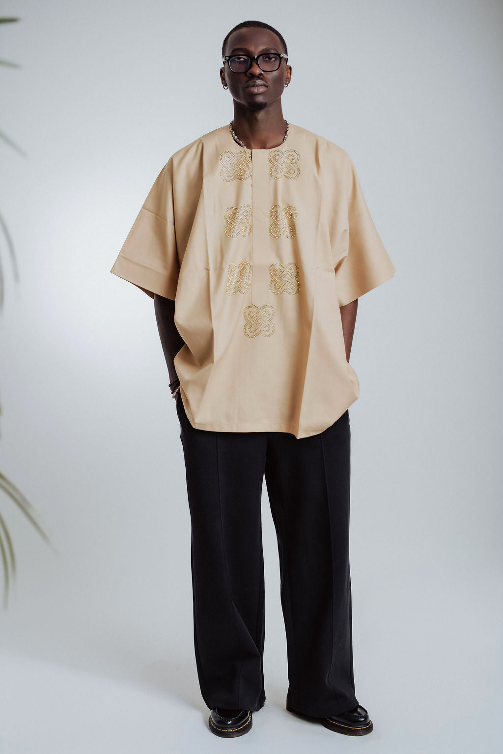 Person wearing a beige embroidered top and black pants on a white background