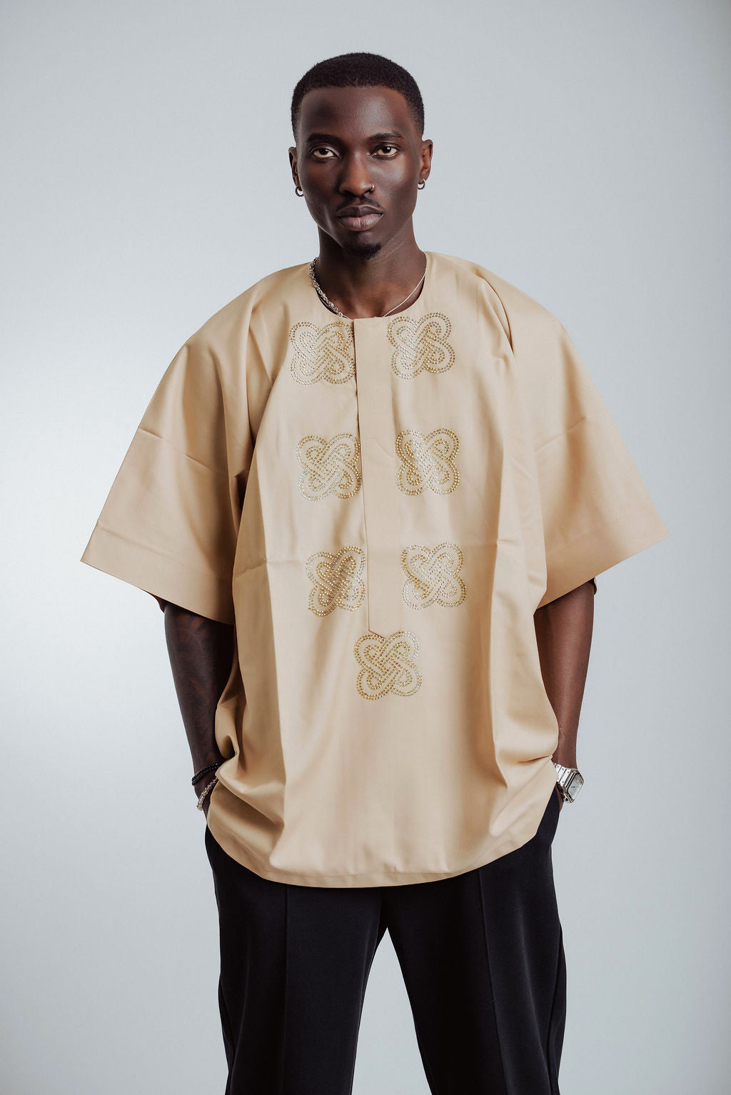 Man wearing a beige embroidered shirt against a white background