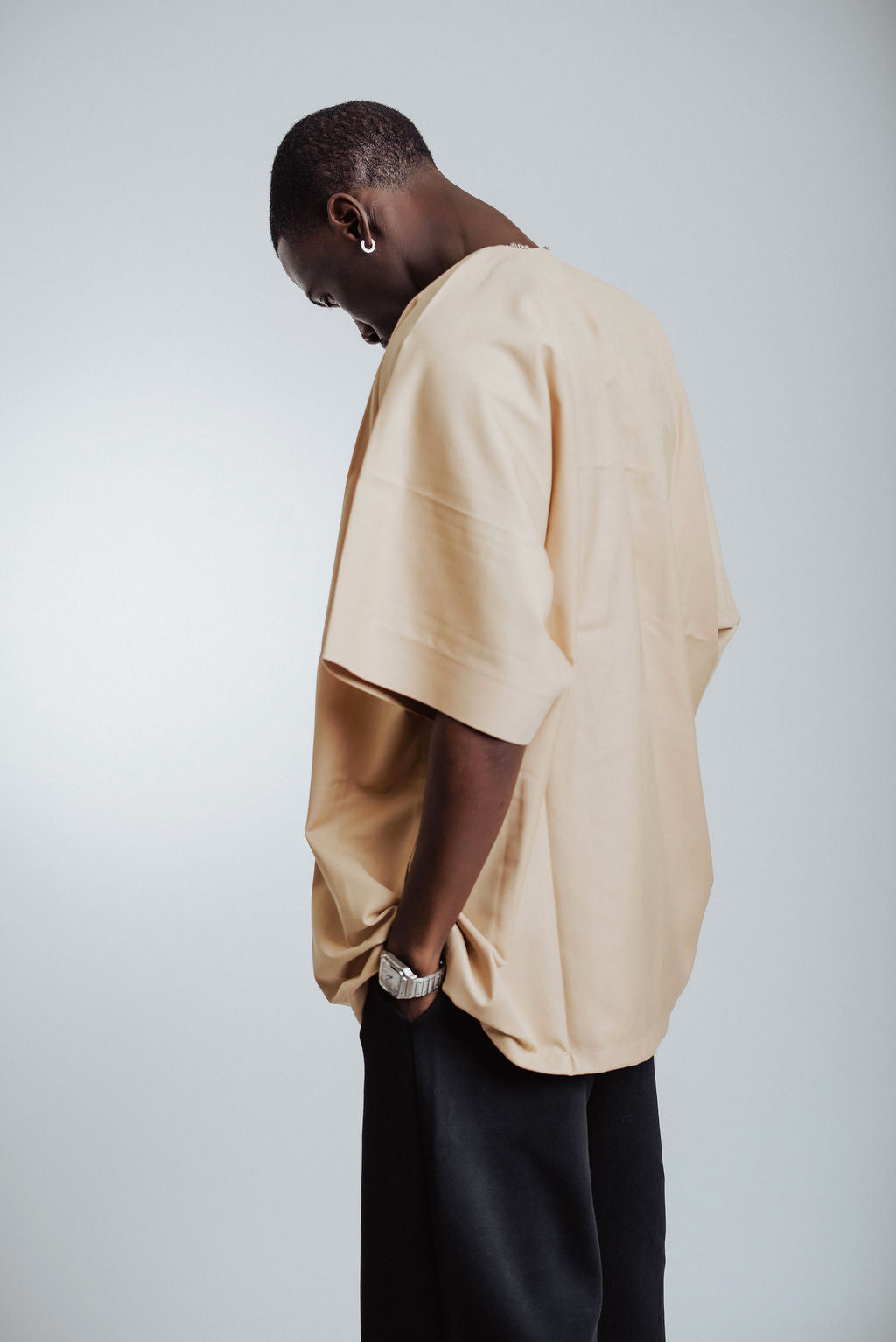 Man wearing a beige oversized shirt and black pants on a light gray background