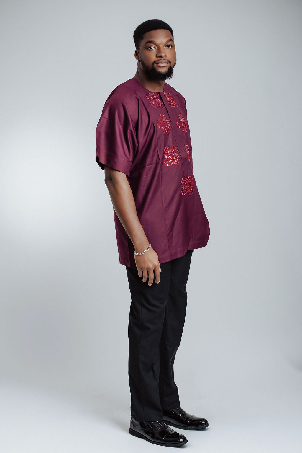 Man wearing a burgundy shirt with red stones and black pants on a white background