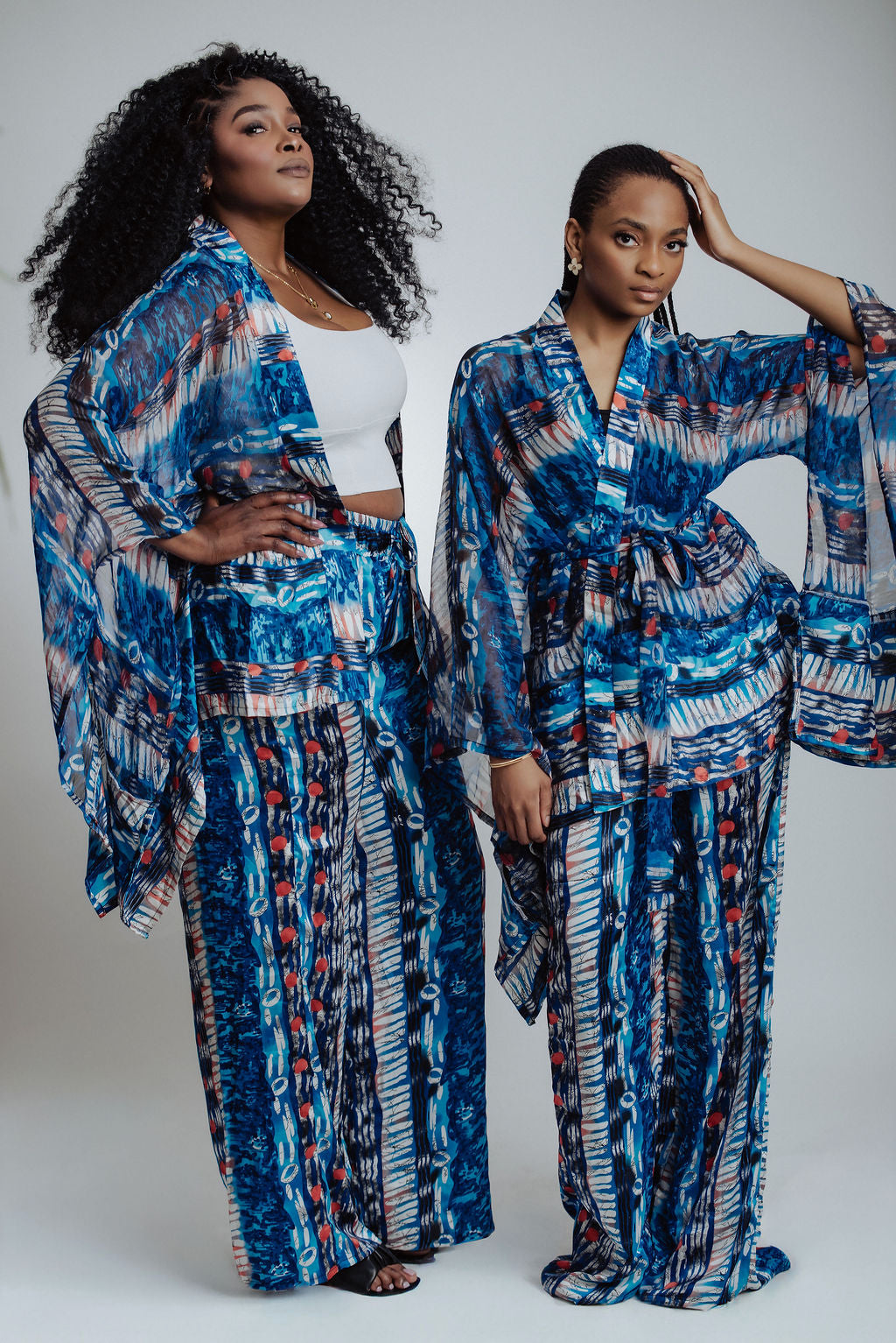 Two women wearing matching blue patterned pants and kimono on a white background