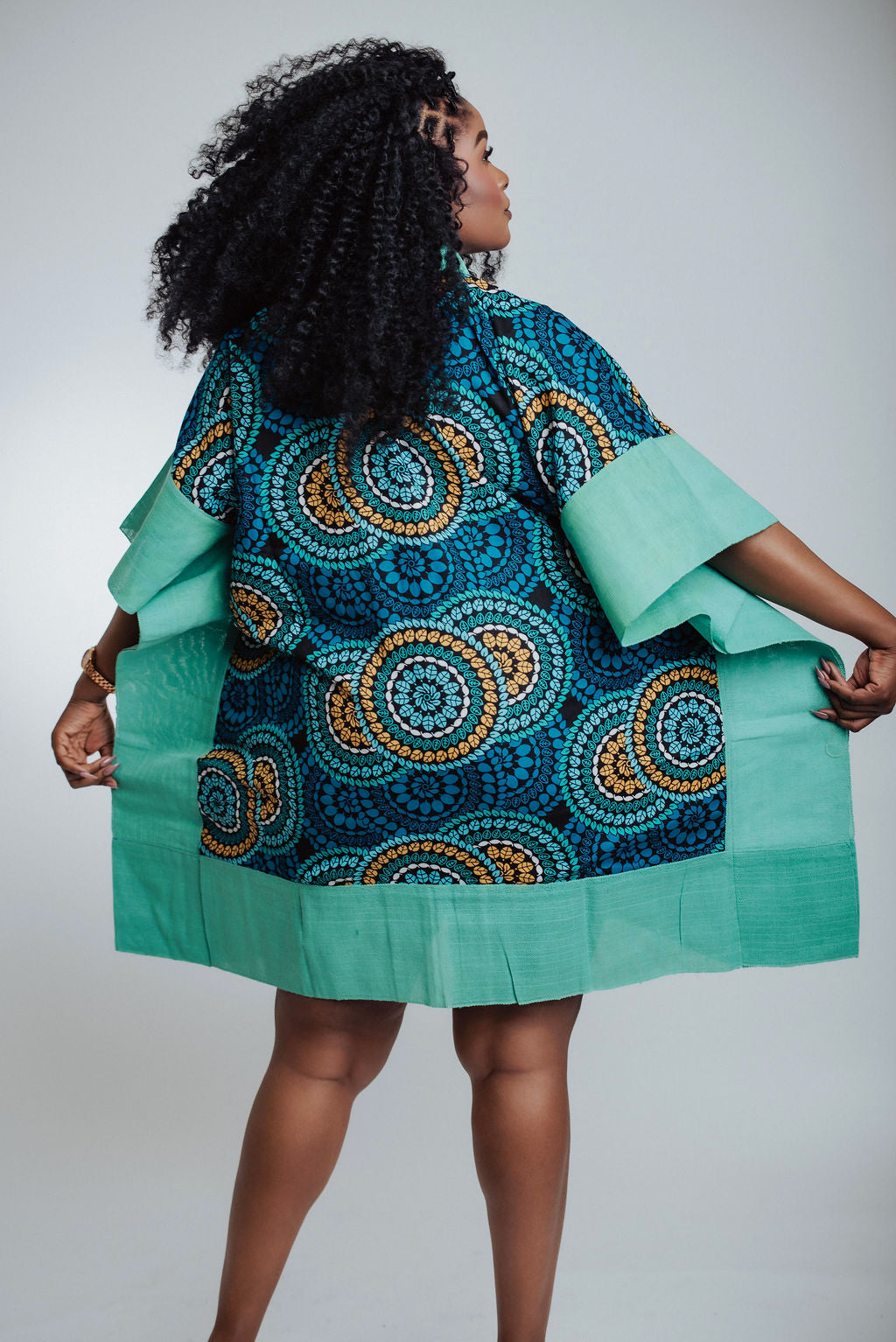 Woman wearing a teal and blue patterned dress against a white background - back view