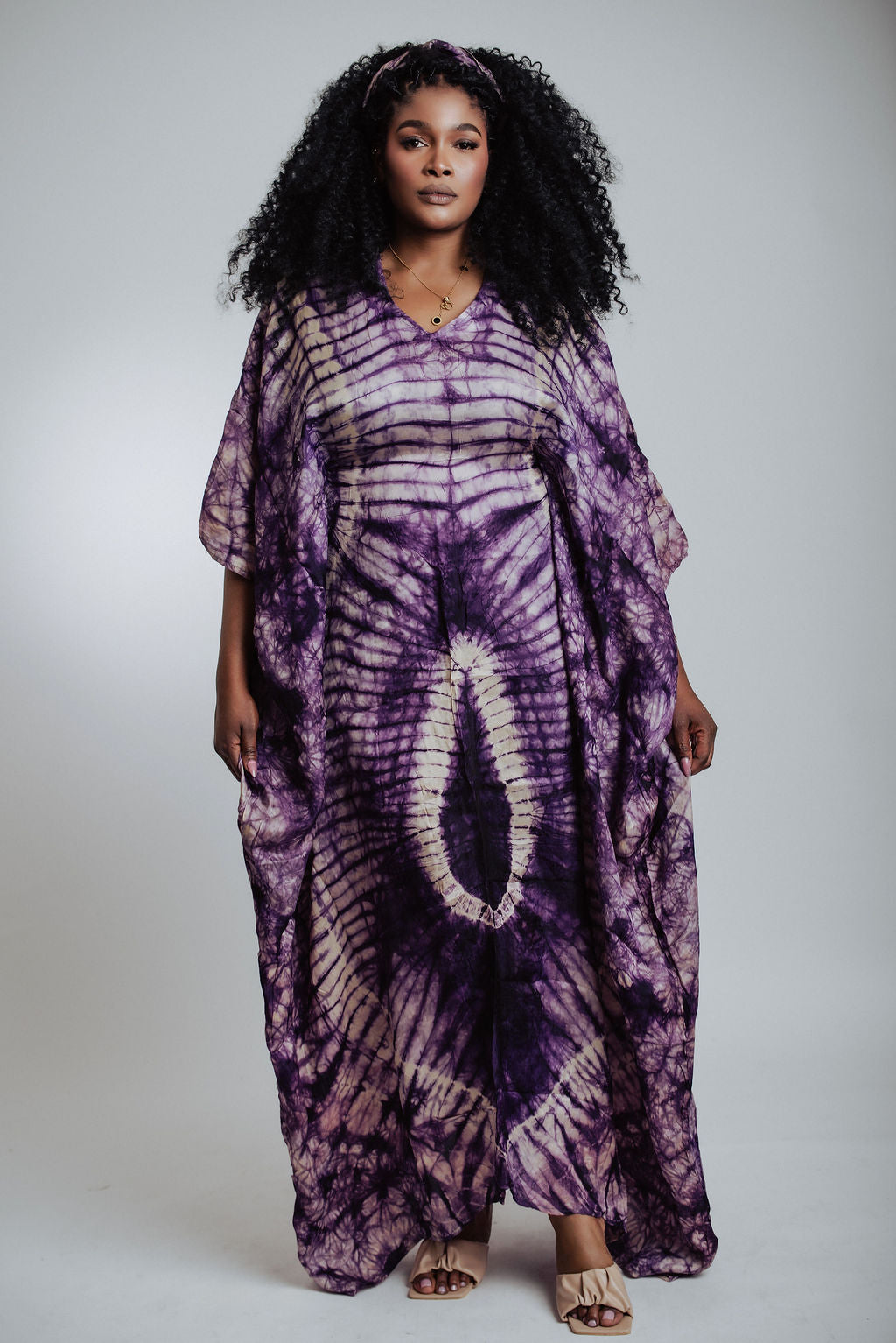 Woman wearing a purple tie-dye dress against a plain background